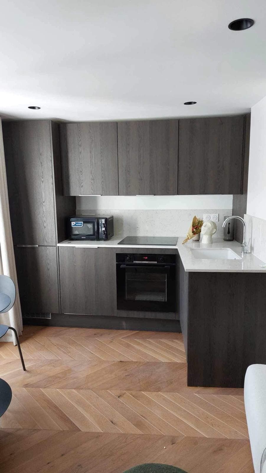 Cuisine en bois foncé avec retour en L, sol en parquet en chevron