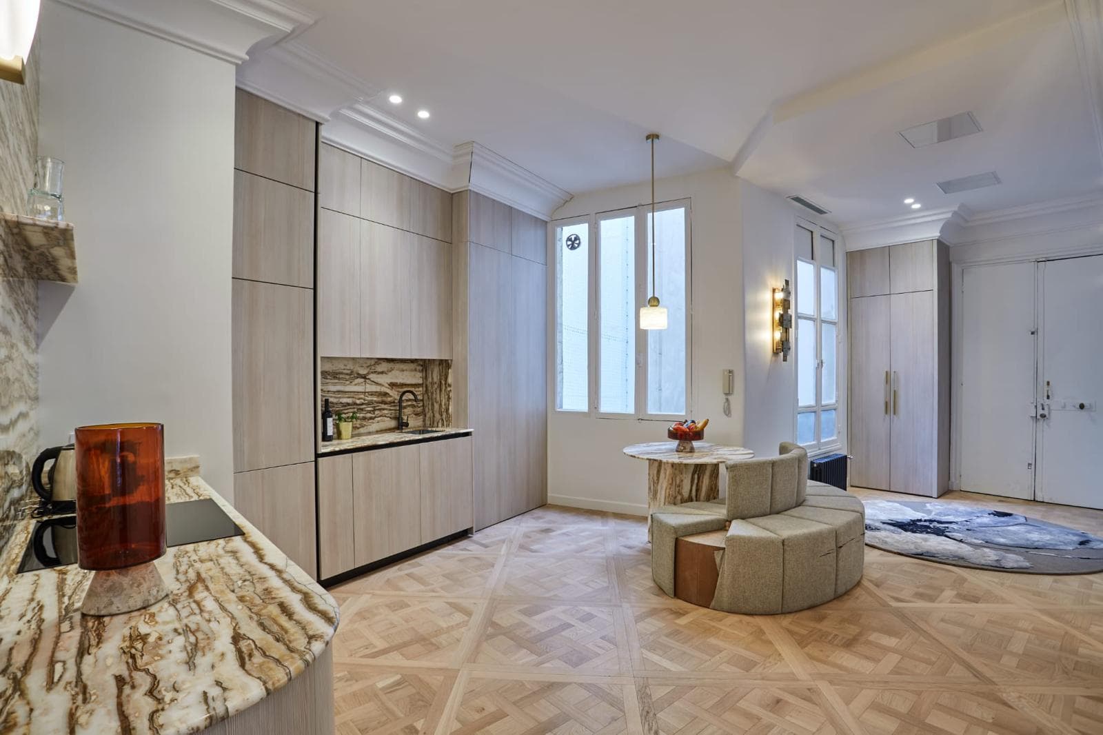 Cuisine intégrée aux façades bois, coin repas avec banquette ronde et parquet Versailles